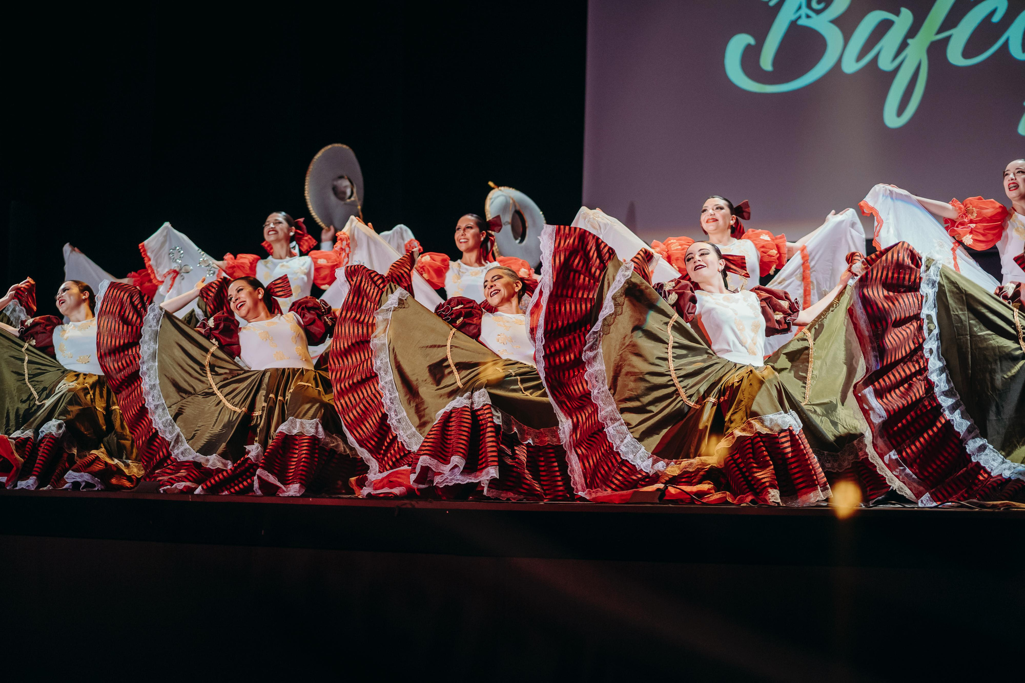 Bailarinas y bailarines del Ballet Folclórico de Coronel en escena, con vestuario tradicional y luz teatral.